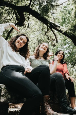 Téléchargez les photos : "Trois jeunes femmes saluant quelqu'un hors caméra dans la forêt, concept d'amitié multiculturelle, concept de bonheur" - en image libre de droit
