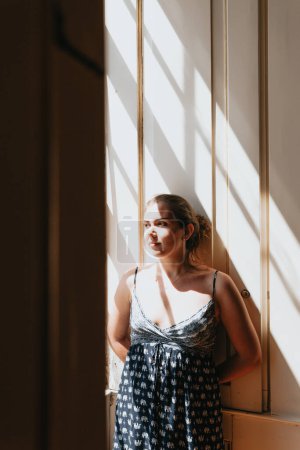 Téléchargez les photos : "Young woman looking through a window during a super sunny day, copy space, reflexion and thinking concept, sad and anxiety, self care" - en image libre de droit