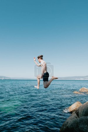 Photo for "Young man jumping into the sea, in the air, mediterranean holidays, freedom and liberty concepts, modern, pale man" - Royalty Free Image
