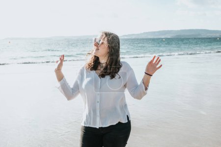 Téléchargez les photos : "Happy young woman laughing and smiling at the beach on a summer day, enjoying vacation, concept of friendship enjoying the outdoor" - en image libre de droit
