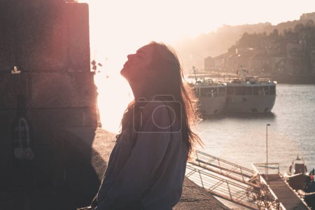 Photo for Woman closing eyes and looking up while exhaling and relaxing in the docks of the city, during a colorful sunset, mental health concept, tourism - Royalty Free Image
