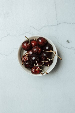 Photo for Aerial image of a dish filled with cherries over a white marble table, fresh food, wellness, healthy food - Royalty Free Image