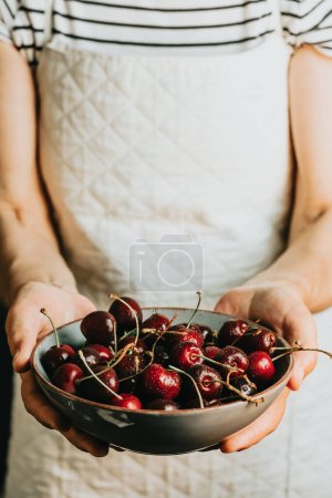 Foto de Old waitress offers and holds a bunch of cherry in a dish, fruits, healthy life, good eating, mediterranean concepts, copy space, vertical image - Imagen libre de derechos
