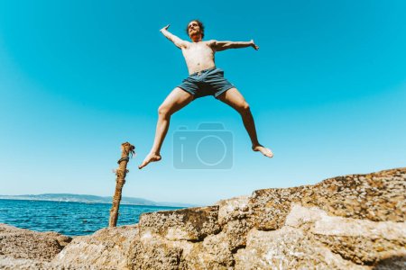 Photo for Young male with long hair jumping in the air, shirtless during a sunny day, space and liberty concept, holidays, fantastic image, beach day - Royalty Free Image