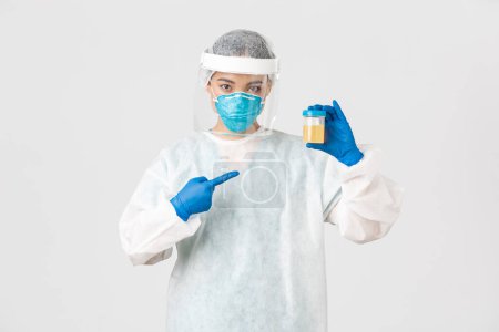 Photo for Covid-19, coronavirus disease, healthcare workers concept. Side view of serious-looking tech lab employee, researcher in personal protective equipment, pointing at urine analyze - Royalty Free Image