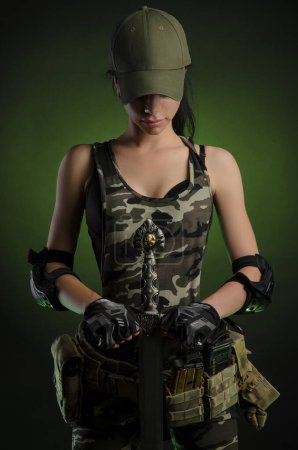 Foto de La chica con ropa militar especial posando con un arma en sus manos sobre un fondo oscuro en la niebla - Imagen libre de derechos