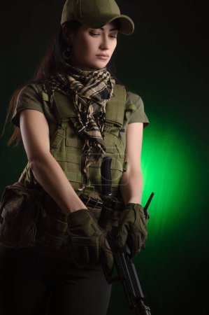 Foto de "la chica con ropa militar especial posando con un arma en sus manos sobre un fondo oscuro en la niebla
" - Imagen libre de derechos