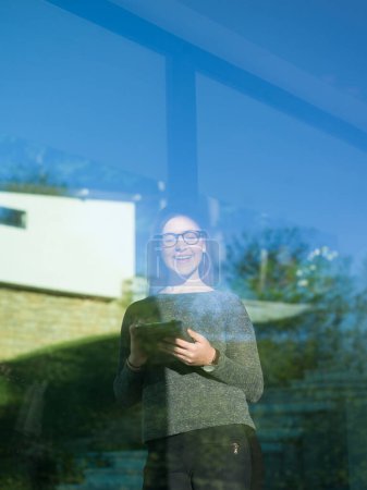 Foto de Mujer usando tableta en casa junto a la ventana - Imagen libre de derechos