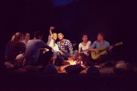 Photo for Young friends relaxing around campfire - Royalty Free Image