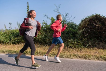 Téléchargez les photos : "jeune couple jogging le long d'une route de campagne" - en image libre de droit