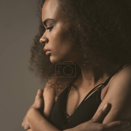 Photo for Square crop. Standing sideways tender African American girl dressed in black top isolated on grey background. Human emotions, facial expression concept - Royalty Free Image