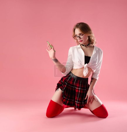 Téléchargez les photos : Fille avec des lunettes dans un costume de professeur écolière sexy sur un fond rose - en image libre de droit