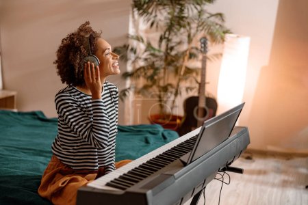 Foto de Mujer alegre en auriculares jugando sintetizador en casa - Imagen libre de derechos