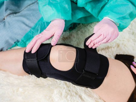 Téléchargez les photos : Gros plan d'un médecin de famille qui met une attelle noire sur le genou d'un patient - en image libre de droit