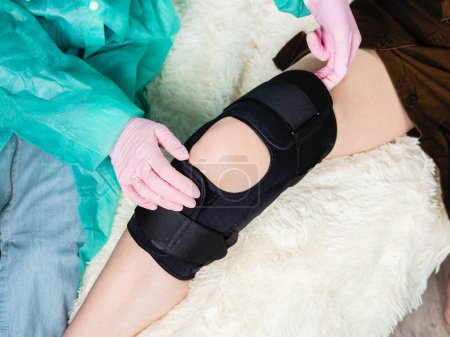 Téléchargez les photos : Gros plan d'un médecin de famille mettant une attelle noire sur le genou d'un patient - en image libre de droit