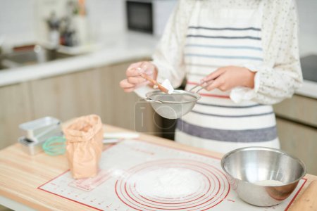Photo for "Mom prepares breakfast. A woman pours flour into a plate. The cooking process. Home kitchen" - Royalty Free Image
