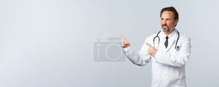 Photo for "Covid-19, coronavirus outbreak, healthcare workers and pandemic concept. Mad annoyed doctor cursing, pointing fingers upper left corner and frowning disapproval, complaining" - Royalty Free Image