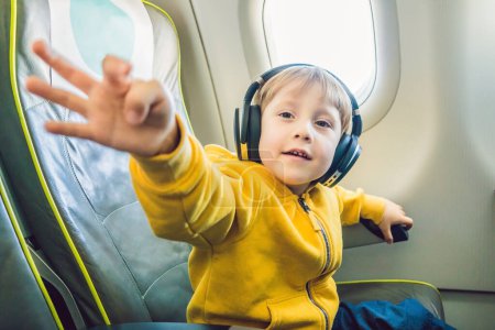 Téléchargez les photos : Garçon avec écouteurs regarder et écouter dans le divertissement de vol à bord de l'avion - en image libre de droit
