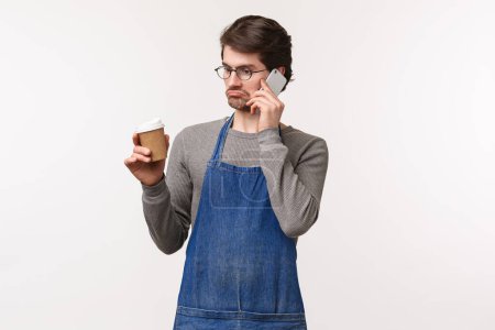 Photo for "Portrait of unsure and indecisive young man having conversation on phone, drink coffee, grimacing puzzled, dont know, cant answer as have no idea, standing confused white background" - Royalty Free Image