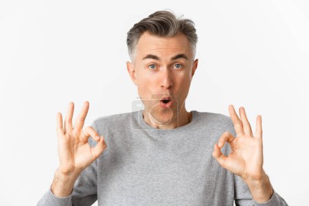 Photo for Close-up of impressed middle-aged guy, showing okay signs in approval, like something good, recommending product, standing over white background - Royalty Free Image