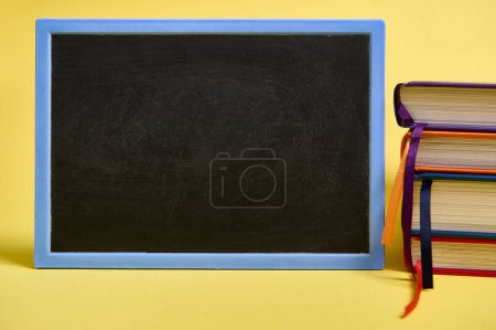 Photo for A blank chalkboard and multicolored books on yellow surface background with copy space for text. Teacher's Day concept, Knowledge, literature ,reading, erudition - Royalty Free Image