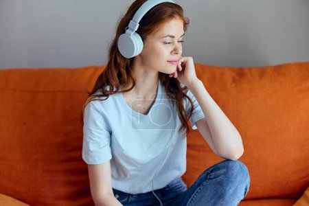 Foto de "hermosa mujer sentada en el sofá en casa escuchando música en las tecnologías de auriculares" - Imagen libre de derechos