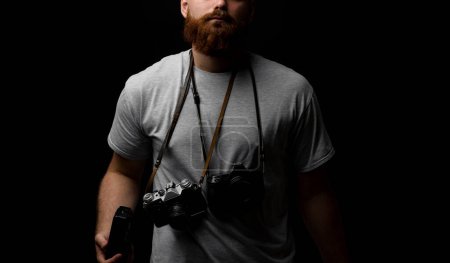 Téléchargez les photos : "Photographe professionnel dans un t-shirt gris avec un tas de caméras différentes sur une épaule." - en image libre de droit