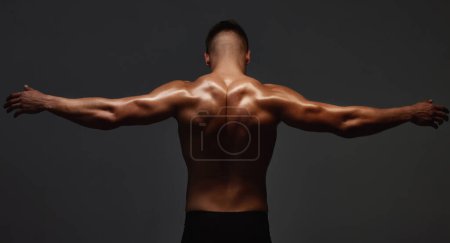 Photo for "Back off. Rearview shot of an unrecognizable and athletic young man posing shirtless in studio against a dark background." - Royalty Free Image