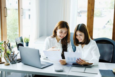 Photo for Consulting, learning, marketing, investment, finance, data analysis, research, two Asian women smiling and holding papers, sitting and analyzing financial statements and using computers at work. - Royalty Free Image