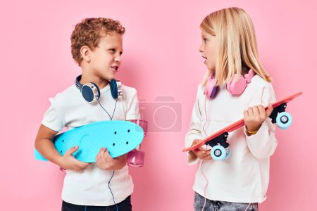 Téléchargez les photos : Petit garçon élégant et jolie fille planches à roulettes dans les mains de divertissement fond isolé - en image libre de droit