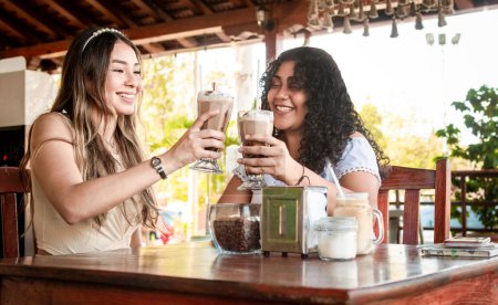 Foto de "Dos chicas tomando un batido, dos amigas en un café, dos chicas brindando en un café" - Imagen libre de derechos