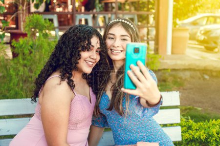 Photo for "Two pretty girls sitting on a bench taking a selfie, girls smiling and taking a selfie, sisterly friendship concept" - Royalty Free Image