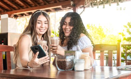 Foto de "Dos chicas tomando una selfie y tomando café, dos chicas amigas con el celular en una cafetería" - Imagen libre de derechos