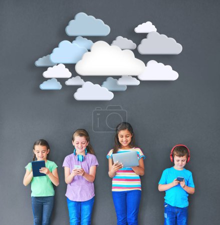 Téléchargez les photos : Les enfants restent connectés. Plan studio d'enfants utilisant la technologie sans fil avec des nuages au-dessus d'eux sur un fond gris. - en image libre de droit