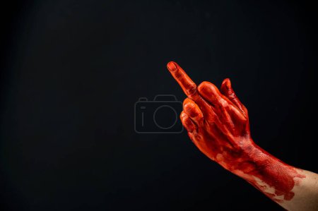 Téléchargez les photos : "Main féminine tachée de sang montre le majeur sur un fond noir." - en image libre de droit