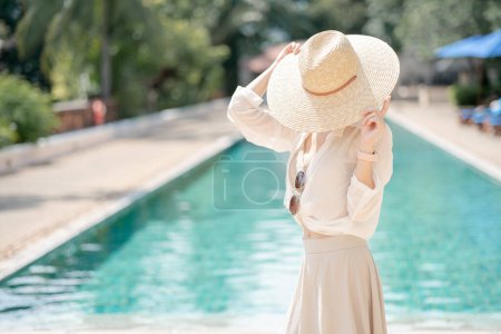 Photo for Woman wearing white shirt, long skirt and straw hat posing near swimming pool. - Royalty Free Image