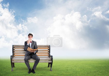Téléchargez les photos : "jeune étudiant portant costume et noeud papillon avec un livre assis sur le banc" - en image libre de droit