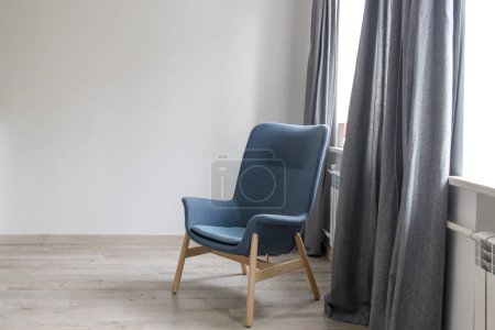 Téléchargez les photos : "Room interior in Scandinavian style, in white and gray tones. A gray armchair with wooden legs by the window." - en image libre de droit