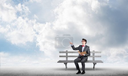 Photo for "young student wearing suit and bow tie with a book sitting on bench" - Royalty Free Image
