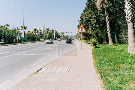 Foto de "Señal de semáforo de pie en el pavimento cerca de la carretera en la ciudad del sur con palmeras en la línea lateral. Detener señal de luz cerca de la carretera ocupada." - Imagen libre de derechos