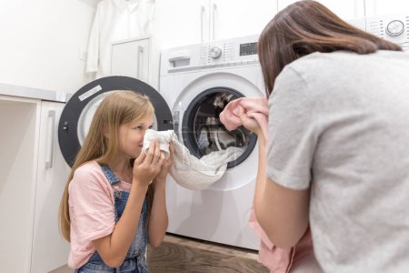 Foto de "Feliz familia madre ama de casa e hija en la lavandería con lavadora y ropa
" - Imagen libre de derechos