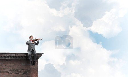 Photo for "Handsome violinist in glasses on building edge play his melody" - Royalty Free Image