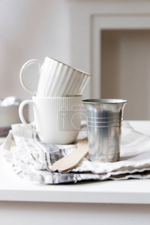 Foto de "Two white mugs, a kitchen towel, a napkin and wooden frying utensils on the table. Defocus." - Imagen libre de derechos