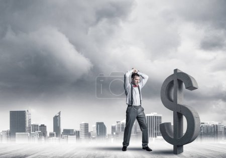 Photo for "Determined banker man against modern cityscape breaking dollar cement figure" - Royalty Free Image