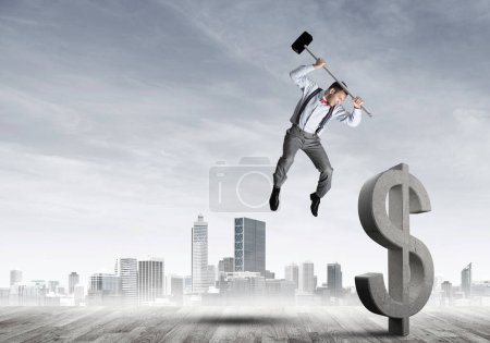 Photo for "Determined banker man against modern cityscape breaking dollar concrete figure" - Royalty Free Image