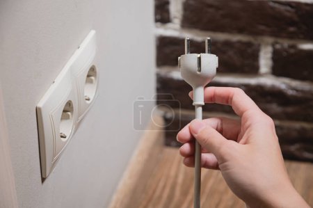 Photo for A female hand inserts white electric plug into a euro-format socket close-up - Royalty Free Image