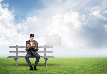 Foto de "joven estudiante vistiendo traje y pajarita con un libro sentado en el banco" - Imagen libre de derechos
