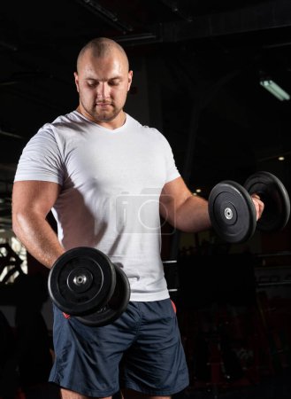 Téléchargez les photos : "bodybuilder masculin engagé avec haltères dans la salle de gym" - en image libre de droit