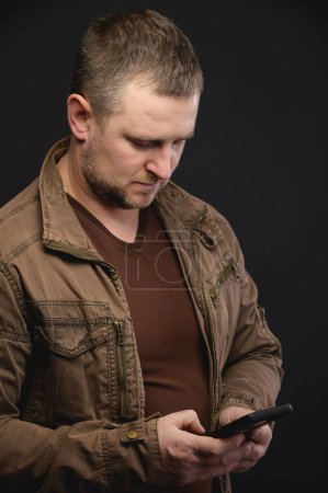 Foto de Hombre caucásico de mediana edad utiliza el teléfono mientras está de pie en el estudio. Retrato de un freelancer navegando por internet - Imagen libre de derechos