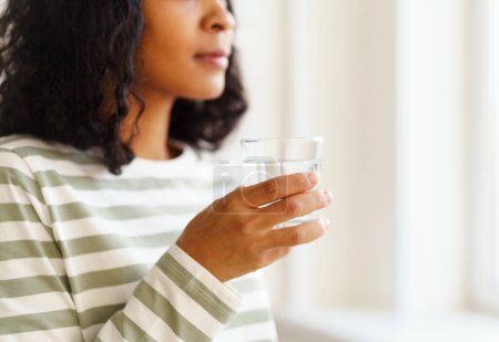 Téléchargez les photos : "Une femme afro-américaine boit un verre d'eau. Début de journée rafraîchissant" - en image libre de droit
